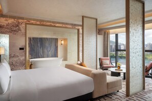 A hotel room with a large bed, a sitting area with a chair and a small table, a bathtub, and a view of the city through large windows. - InterContinental Shenzhen ICSZ (Shenzhen)