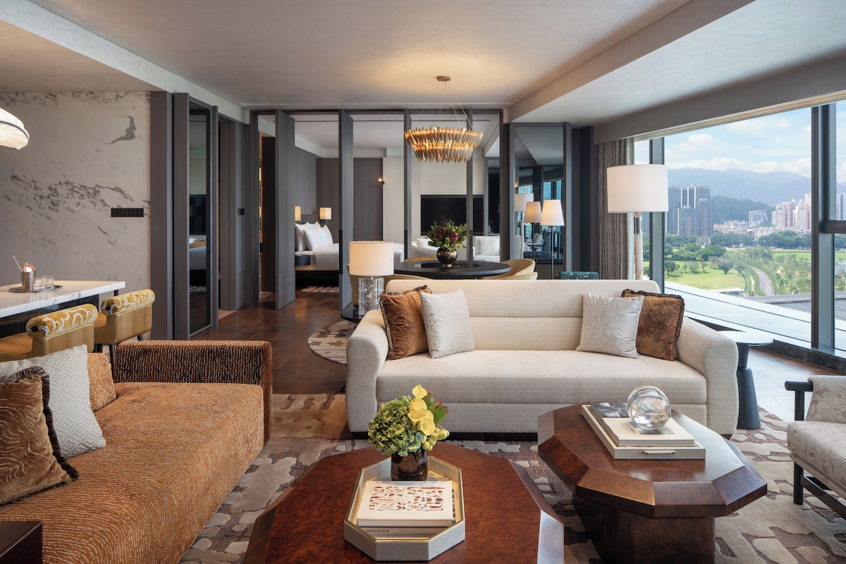 Ein modernes Hotelzimmer mit einer Couch, Sesseln, einem Couchtisch und Blick auf die Stadtlandschaft.