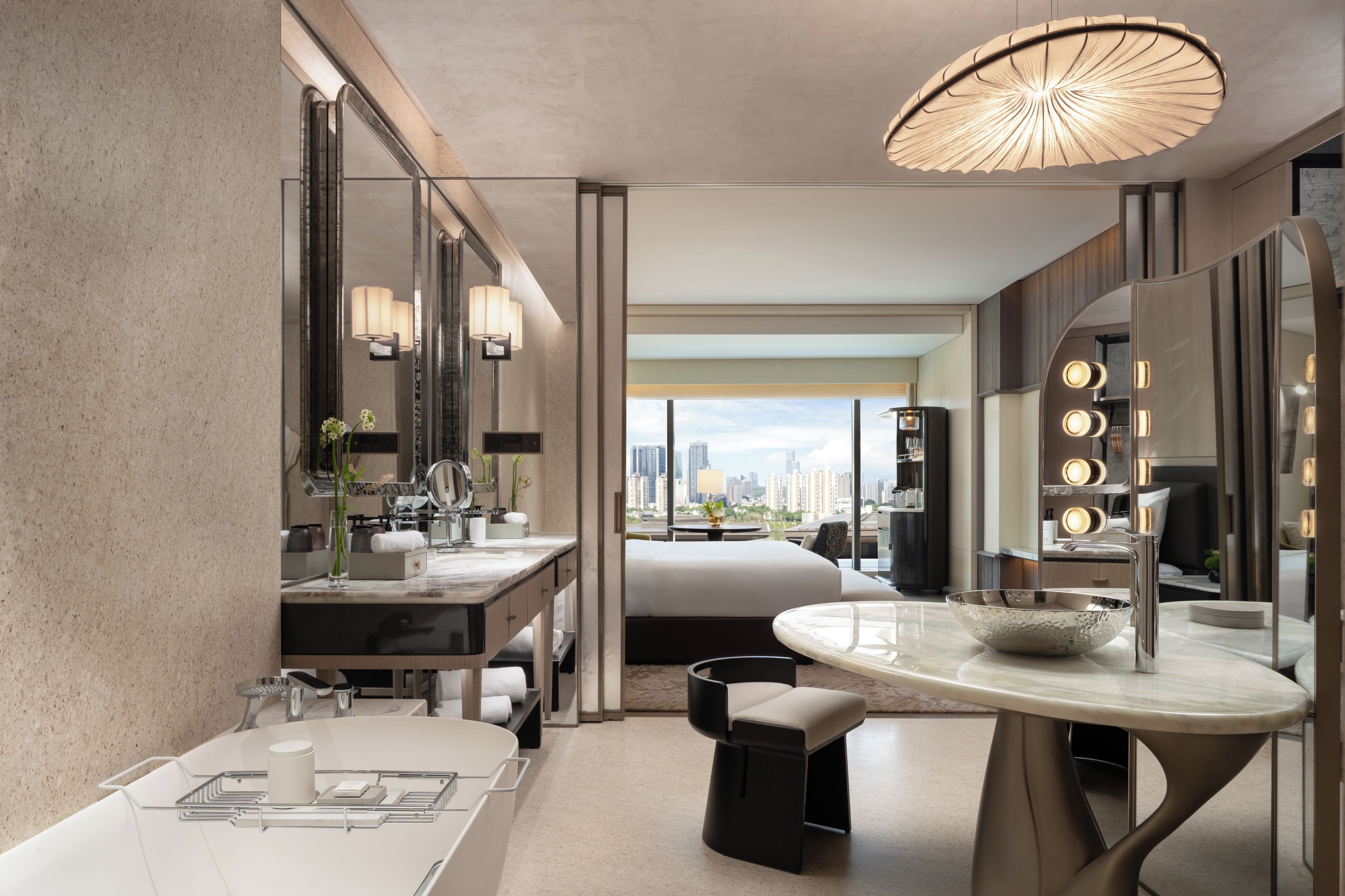 A modern hotel bathroom with a large mirror, vanity, and a view of the cityscape.