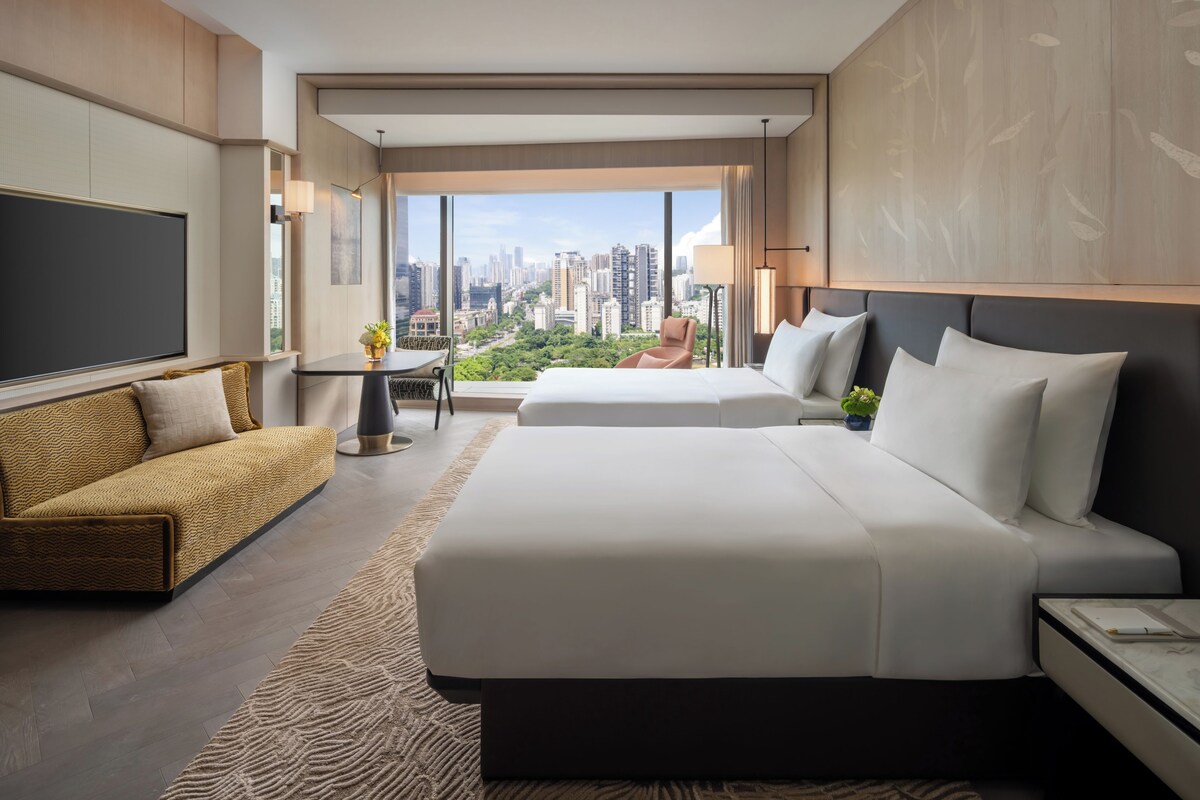 Ein Hotelzimmer mit einem großen Bett, einem Sofa, einem Schreibtisch und Blick auf eine Stadtlandschaft.