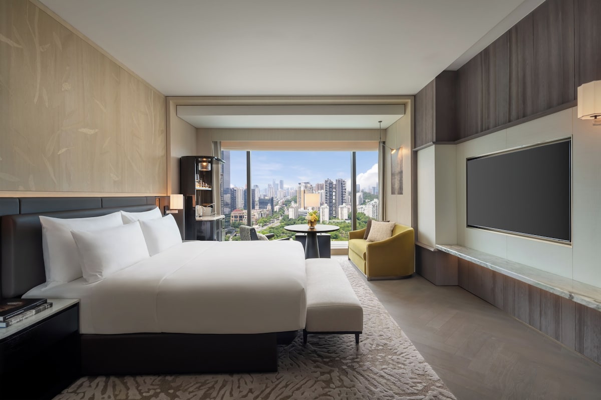 Ein modernes Hotelzimmer mit einem großen Bett, einer Sitzecke, einem Fernseher und Blick auf die Stadt.