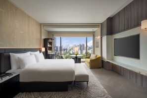 Habitación de hotel moderna con una cama grande, zona de estar, televisor y vistas a la ciudad.