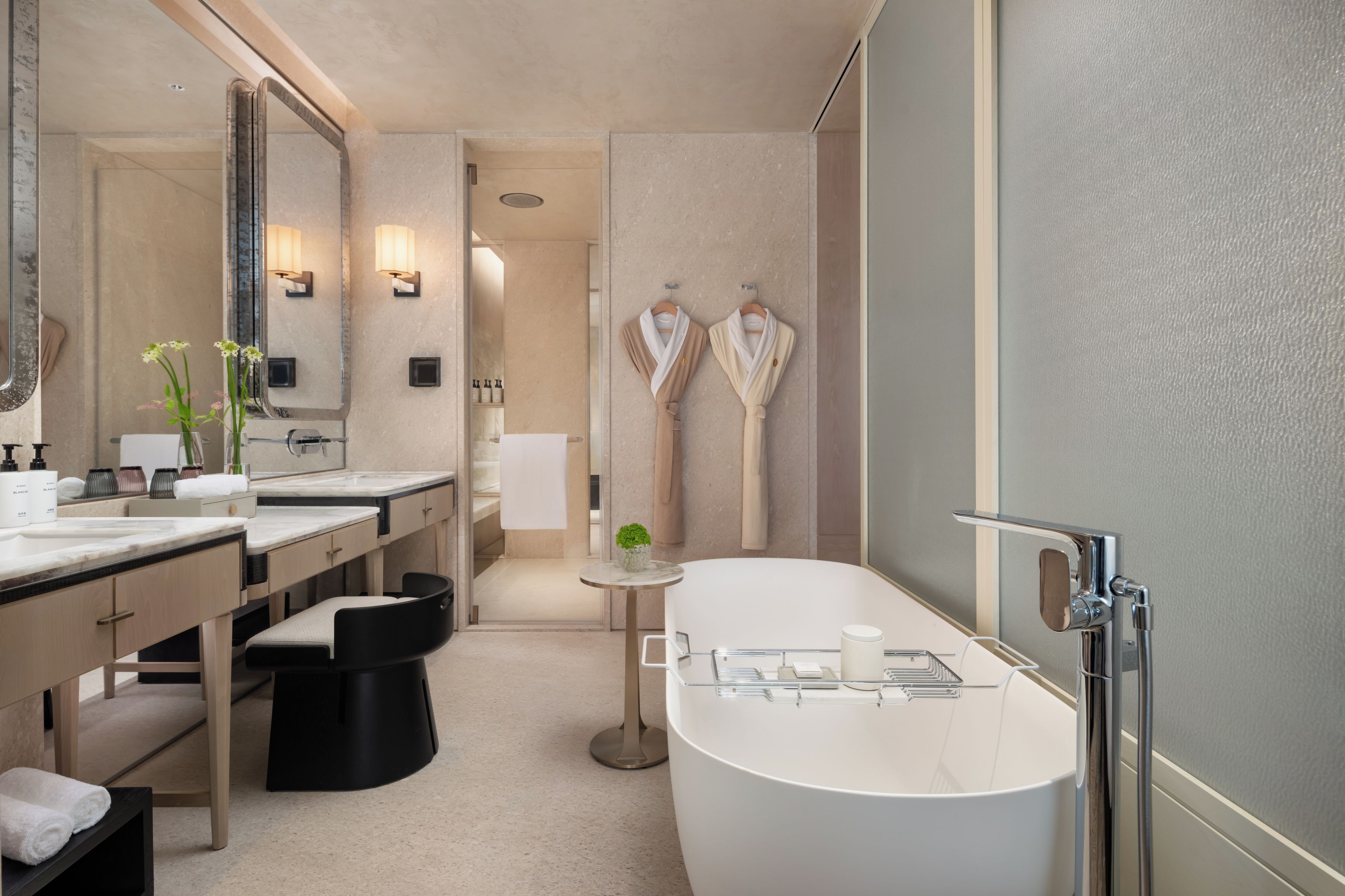 Une salle de bain moderne avec une grande baignoire, deux lavabos, un meuble-lavabo avec un miroir et une petite table ronde agrémentée d’une plante.