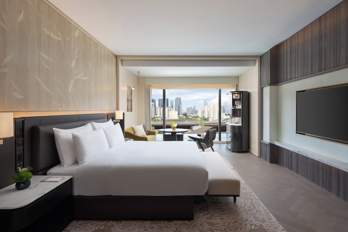 Ein modernes Hotelzimmer mit einem großen Bett, einer Sitzecke, einem Fernseher und Blick auf die Stadt.