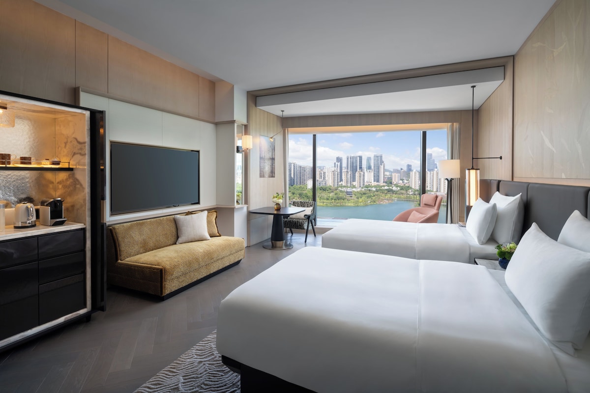 Ein modernes Hotelzimmer mit einem großen Bett, einer Sitzecke, einem Fernseher und Blick auf die Stadt.