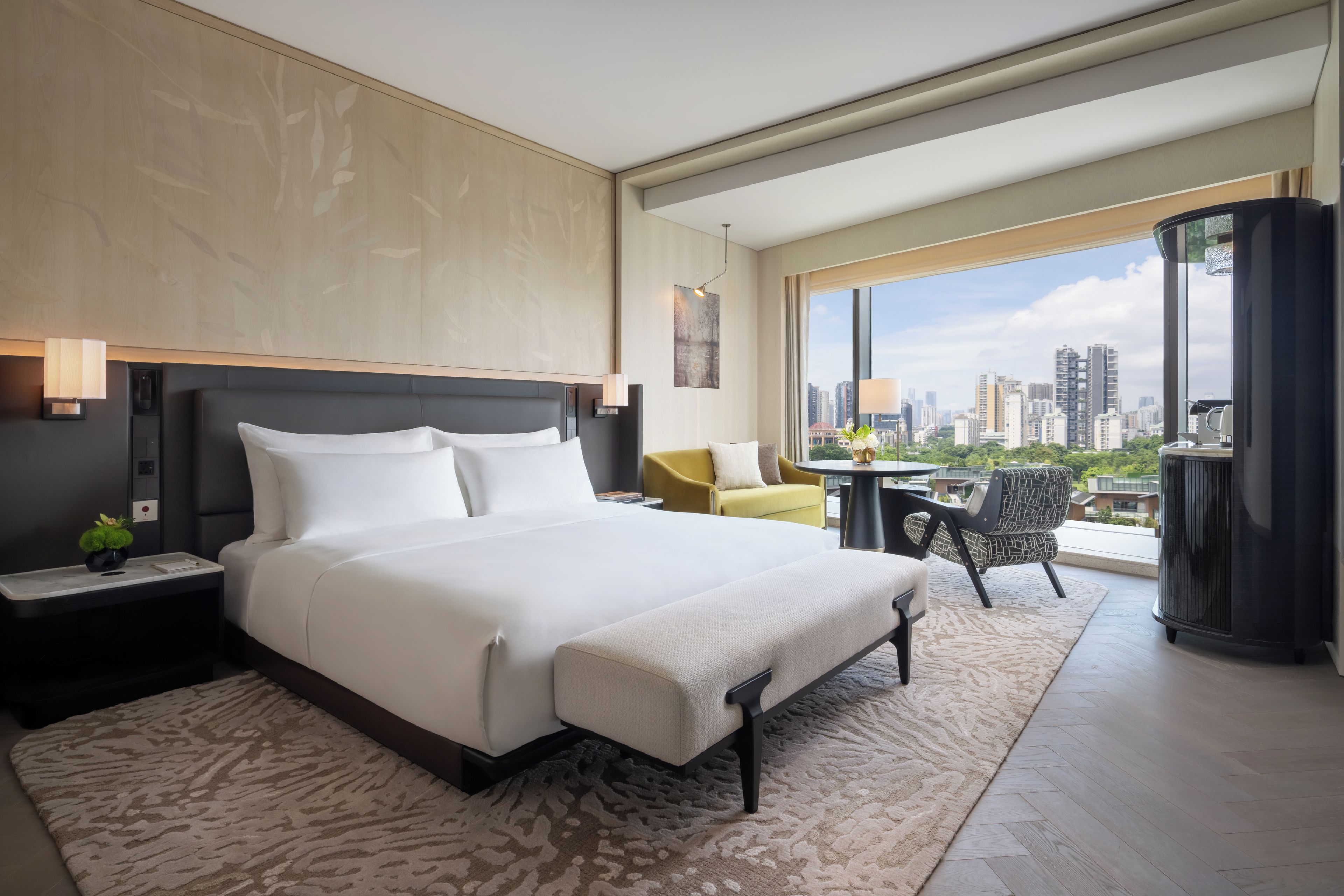 Una camera d'albergo moderna con un letto grande, un tavolino, un divano e un balcone con vista sulla città.
