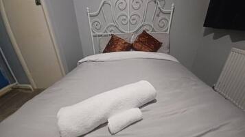 Una cama con cabecera blanca, dos almohadas y dos toallas enrolladas.