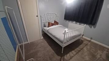 A bedroom with a single bed, a radiator, a door, and a window with curtains.
