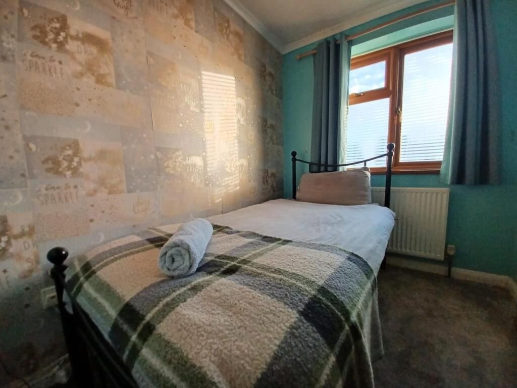 A room with a bed, a window with curtains, and a wall with a unique pattern.