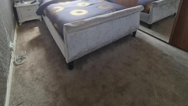 Een slaapkamer met een bed, nachtkastje, lamp, raam met gordijnen en een spiegel.