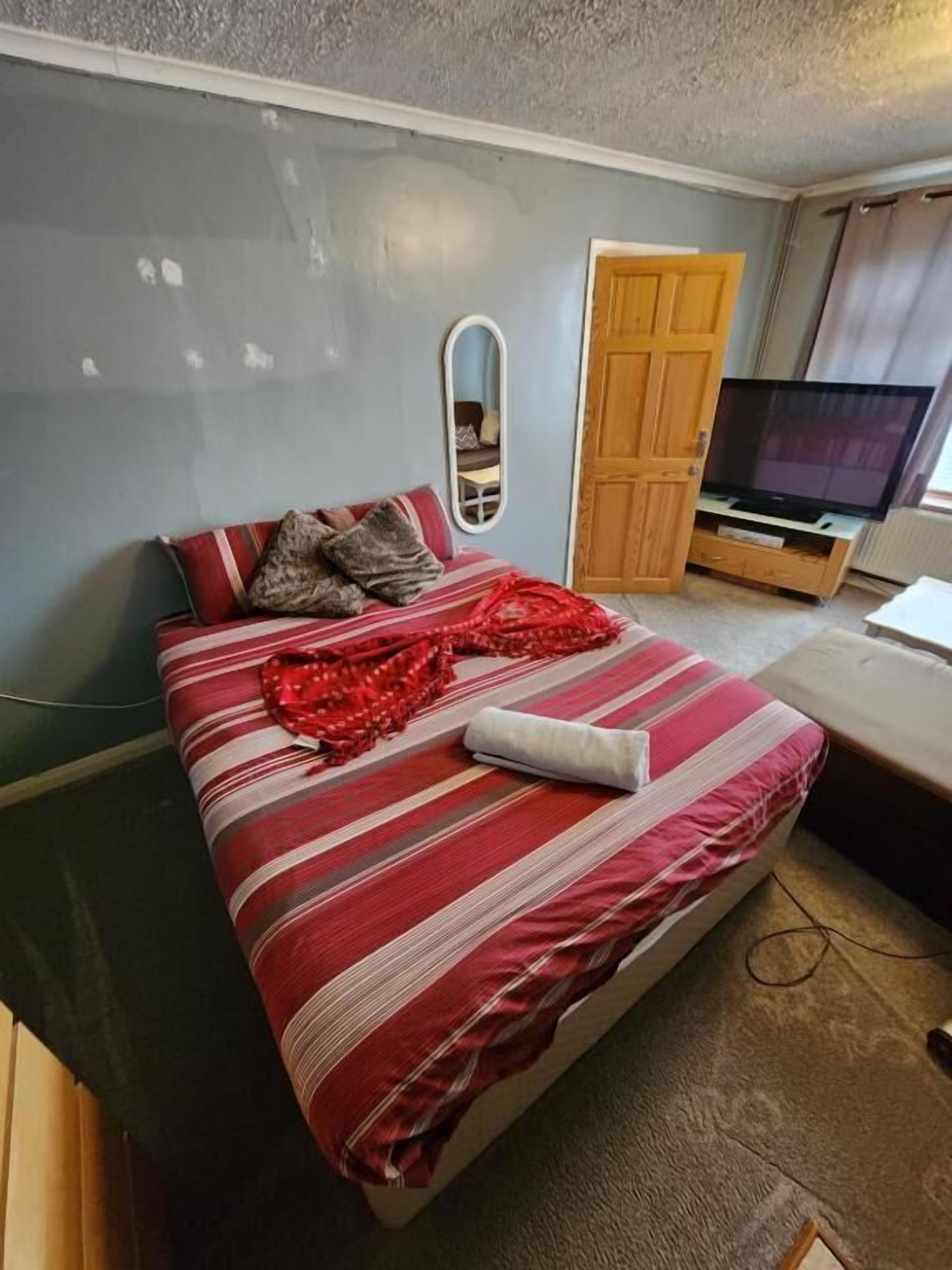 A bedroom with a bed, a television, a wardrobe, and a mirror.
