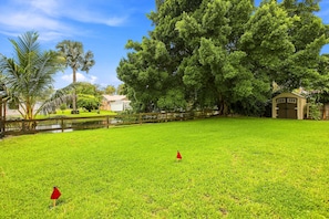 A grassy area with a wooden fence, a small pond, and a large tree. - Waterfront Paradise with hot tub, near 5th Ave (Naples)