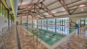 An indoor swimming pool with clear lanes, a diving board, and a seating area along the side.