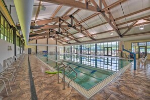 An indoor swimming pool with clear lanes, a diving board, and a seating area along the side.