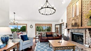 A spacious living room with a fireplace, a chandelier, and a view of the outdoors.