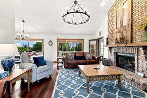 A spacious living room with a fireplace, a chandelier, and a view of the outdoors.