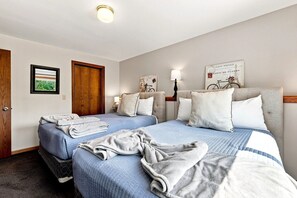 A hotel room with two beds, a wooden wardrobe, a framed picture, and a wall-mounted lamp.