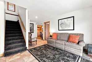 A living room with a staircase, a sofa set, and a framed map on the wall.