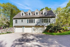 A two-story house with a garage, a stone wall, and a driveway. - Lands End House at Cape Porpoise with Hot Tub (Kennebunkport)