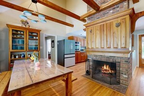 A spacious kitchen with a fireplace, wooden cabinets, and a dining table. - Lands End House at Cape Porpoise with Hot Tub (Kennebunkport)