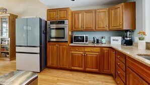 A kitchen with wooden cabinets, a stainless steel refrigerator, a microwave, and a bread box. - Lands End House at Cape Porpoise with Hot Tub (Kennebunkport)