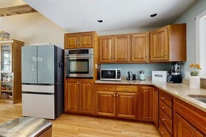 A kitchen with wooden cabinets, a stainless steel refrigerator, a microwave, and a bread box. - Lands End House at Cape Porpoise with Hot Tub (Kennebunkport)