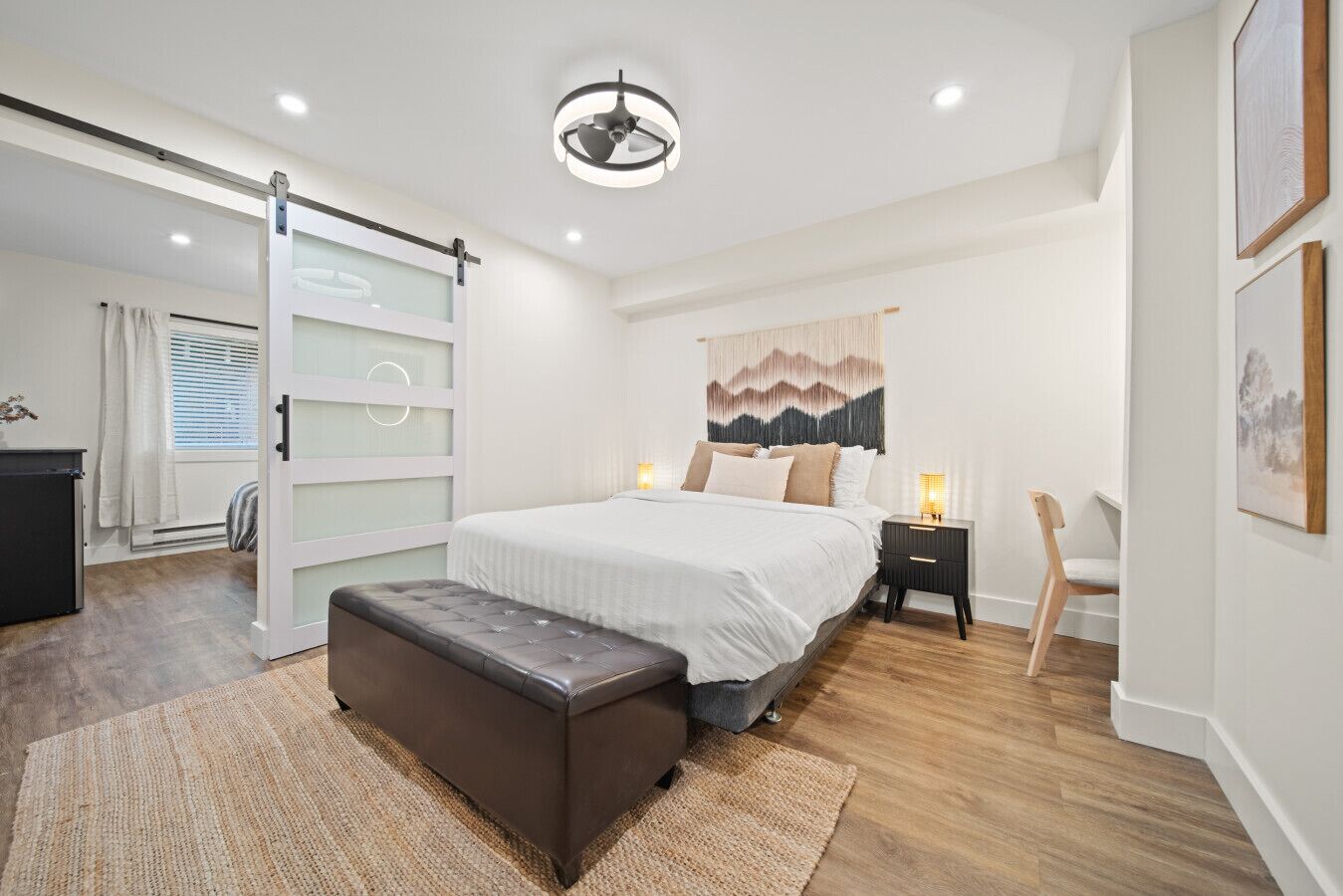 Ein modernes Schlafzimmer mit einem großen Bett, Nachttischen, einer Bank und einer Schiebetür zu einem anderen Raum.