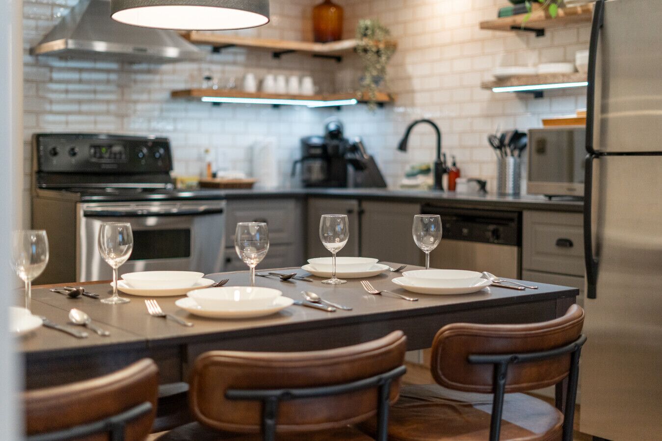 Uma cozinha moderna com uma ilha central, eletrodomésticos de aço inoxidável e uma área de jantar com cadeiras e mesa posta para quatro pessoas.