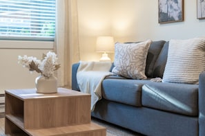 Ein Wohnzimmer mit einer Couch, einem Beistelltisch mit Blumen und einer Lampe.