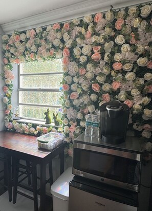 A kitchen with a microwave, a water dispenser, and a coffee maker on the counter. There is a window with a view of greenery outside. - The Enchanted Garden Suite (Pinellas Park)