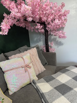 A room with a sofa, pillows, and a decorative tree with pink flowers. - The Enchanted Garden Suite (Pinellas Park)