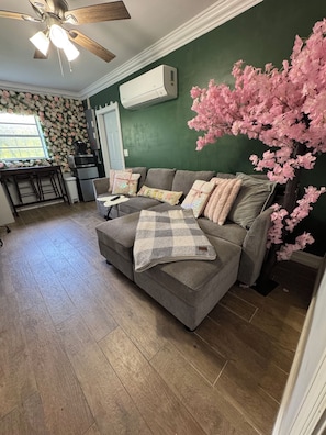 A living room with a grey sofa, a coffee table, and a decorative tree. - The Enchanted Garden Suite (Pinellas Park)