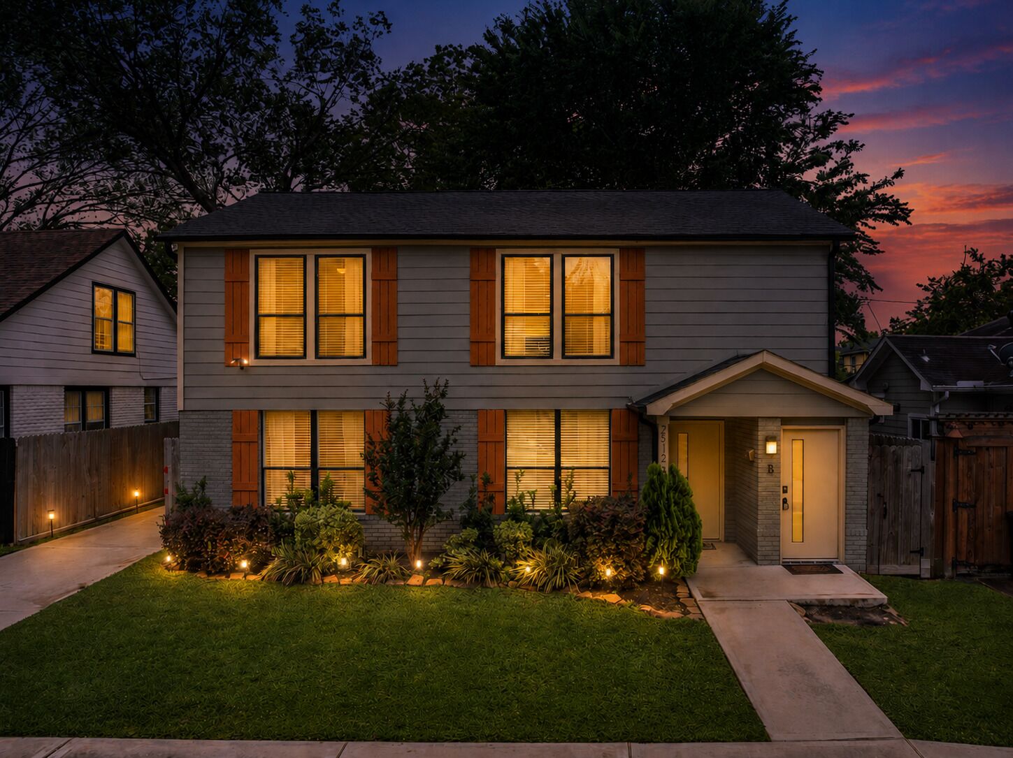 A two-story house with a front porch, a well-maintained lawn, and a wooden fence.