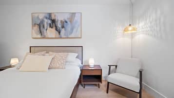 A bedroom with a bed, bedside tables, a chair, a hanging lamp, and a painting on the wall.