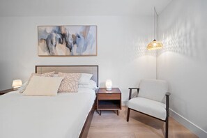A bedroom with a bed, bedside tables, a chair, a hanging lamp, and a painting on the wall. - The Alpine Alcove w Pool & Hot Tub (Whistler)