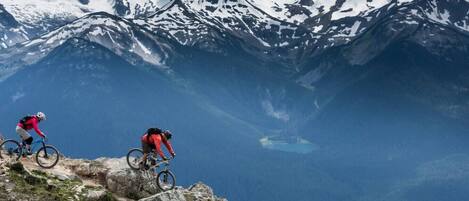 Two mountain bikers on a rocky trail with snow-capped mountains in the background.