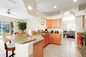 A modern kitchen with granite countertops, wooden cabinets, and a dining area with chairs. - Peaceful Private View Disney Villa Pool Spa (Davenport)