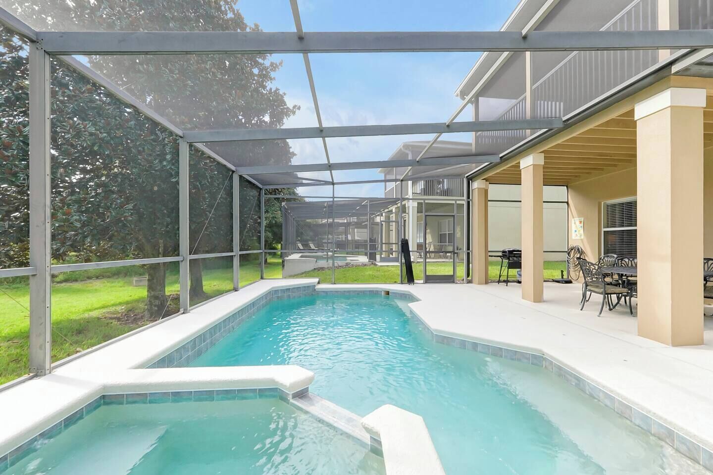 A swimming pool with a covered patio area, outdoor furniture, and a view of a residential building.