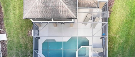 A residential property with a swimming pool, a covered patio area, and a fenced yard.