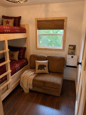 A bunk bed with red bedding and a window with a view of greenery.
