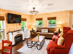 A cozy cabin interior with a fireplace, a sofa, a dining table, and a television mounted on the wall.