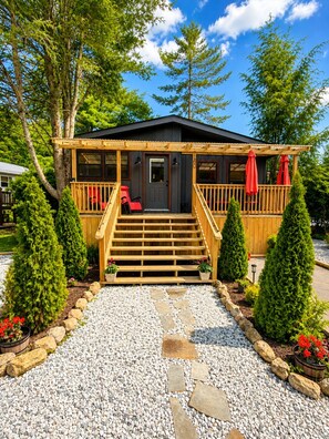 Eine Holzhütte mit Veranda, Treppen zum Eingang und einem Kiesweg.