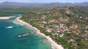 Vista aérea de un pueblo costero con playa, edificios y montañas al fondo.