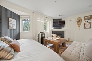 Une chambre à coucher moderne avec un lit, une télévision, une cheminée et une grande fenêtre.