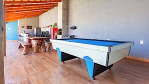 Una mesa de billar en una habitación con suelo de madera, pared de piedra y techo con vigas de madera.