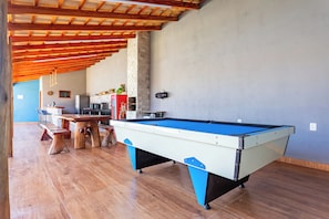 Una mesa de billar en una habitación con suelo de madera, pared de piedra y techo con vigas de madera.