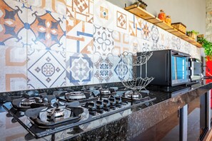 Una cocina con estufa a gas, microondas y una variedad de azulejos estampados en la salpicadera.