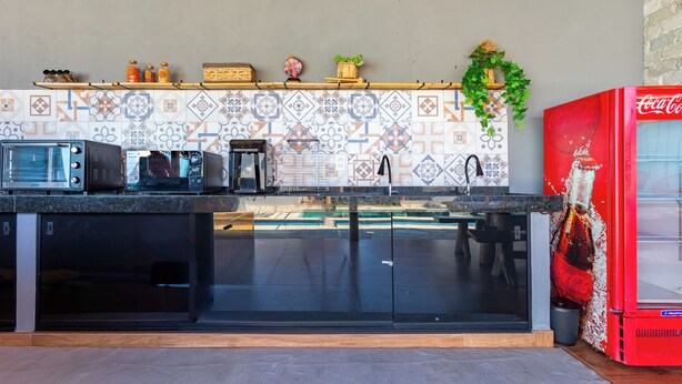 Una cocina con microondas, tostadora y lavabo. Hay un refrigerador rojo y un salpicadero de azulejos.