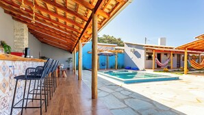 Un espacio al aire libre techado con piscina, asientos de bar y una hamaca.