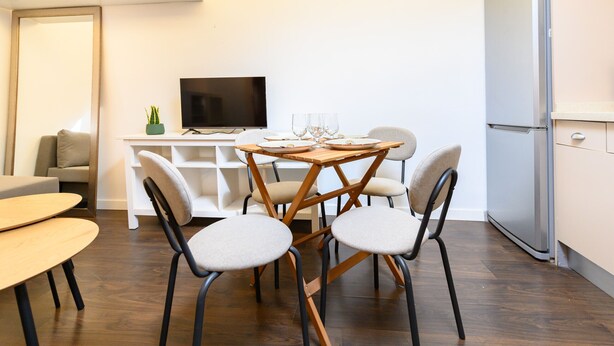 A modern living space with a dining table, four chairs, a television, and a refrigerator. - (FER3452) 1 bedroom penthouse in Moncloa (Madrid)